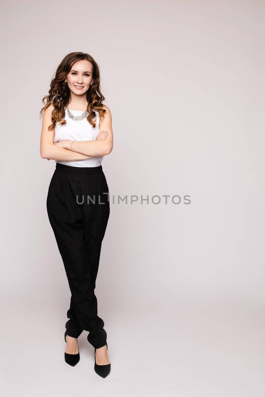 Front view of elegant successful female wearing smart outfit and glasses and posing on isolated background. Intelligent woman with folded arms looking at camera in studio. Concept of job and business.