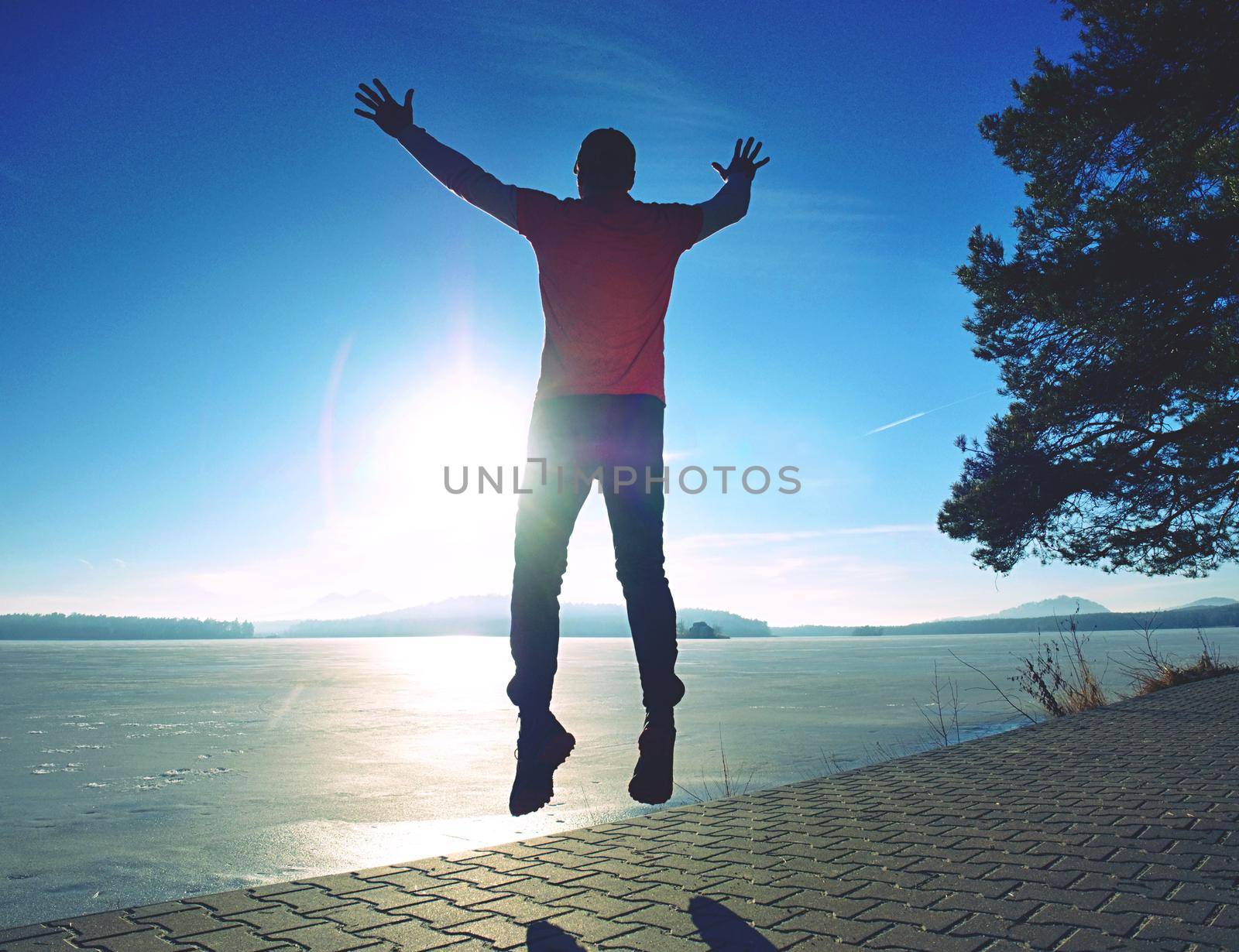 Tall man jamping by sea on the beach. Powerful runner training outdoor in cold spring morning. Hot Sun is rising up over water level