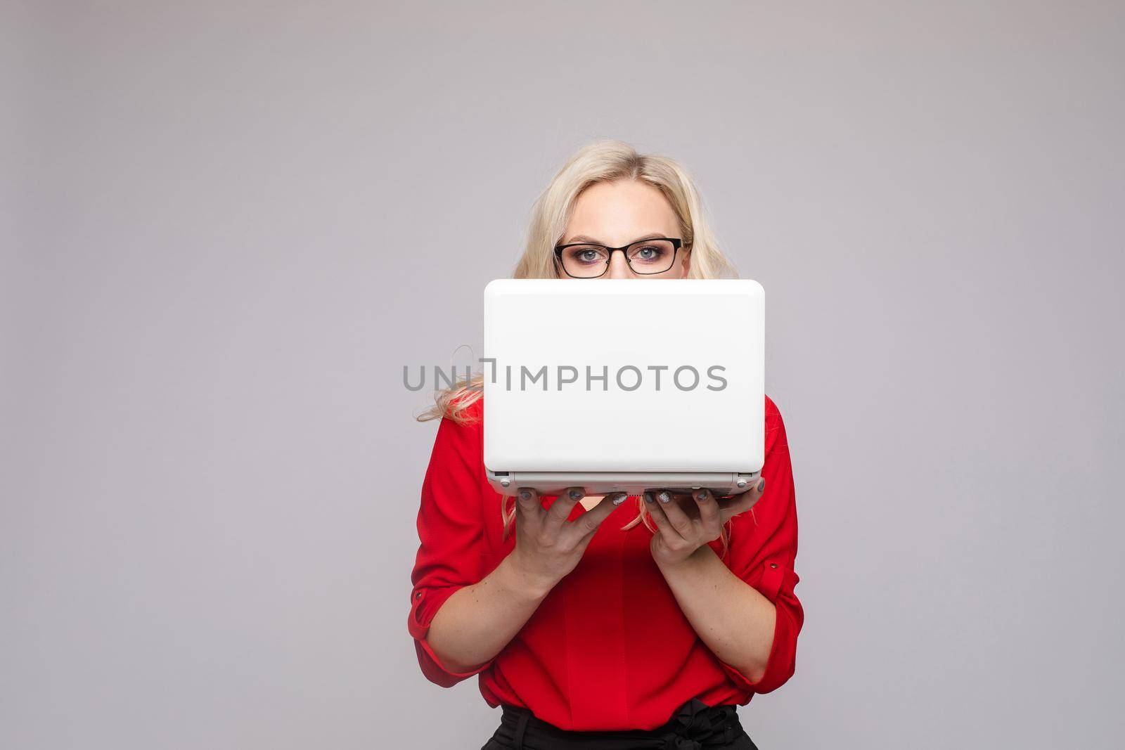 Front view of shocked woman wearing official clothes and glasses keeping computer. Amazed young businesswoman with open mouth looking at camera on isolated background. Concept of surprise.