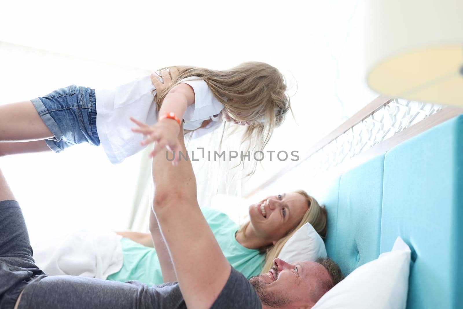 Portrait of father throws kid in air and play, family chill in bed, happy and healthy relationship in family. Parenthood, childhood, quality time concept