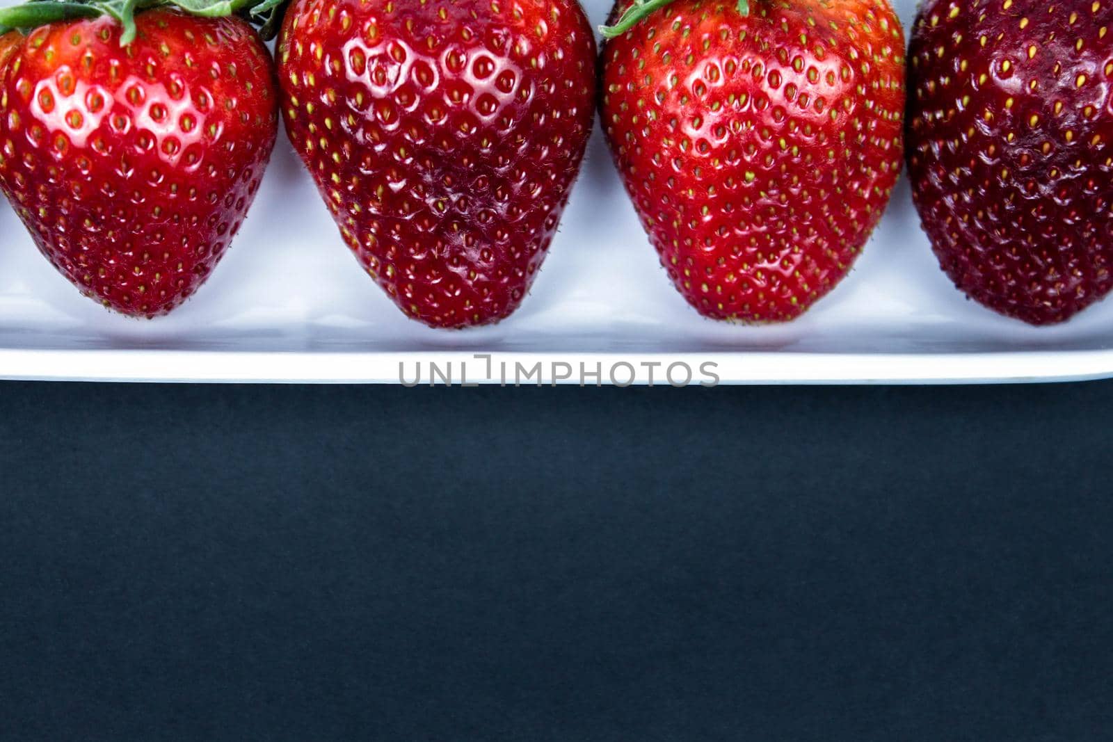 Strawberry in a white plate close up on a black background. Fresh red strawberry in white bowl on black background. side view, copy space, close up by JuliaDorian