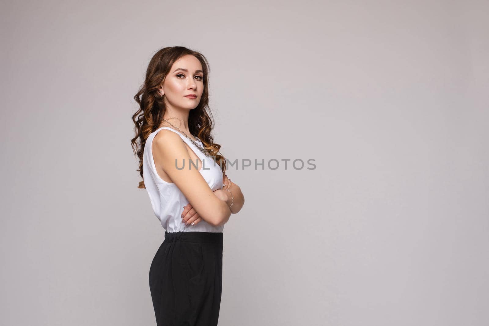 Front view of elegant successful female wearing smart outfit and glasses and posing on isolated background. Intelligent woman with folded arms looking at camera in studio. Concept of job and business.