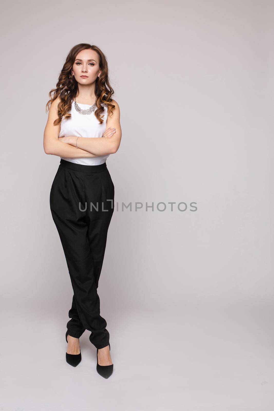 Front view of elegant successful female wearing smart outfit and glasses and posing on isolated background. Intelligent woman with folded arms looking at camera in studio. Concept of job and business.