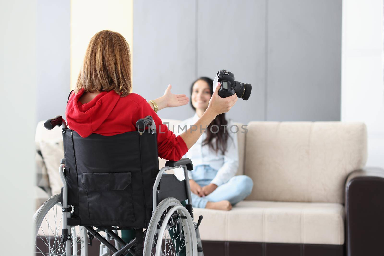 Portrait of professional photographer in wheelchair give advice on posing to model on sofa. Creative artist with photocamera. Disabled people, art concept