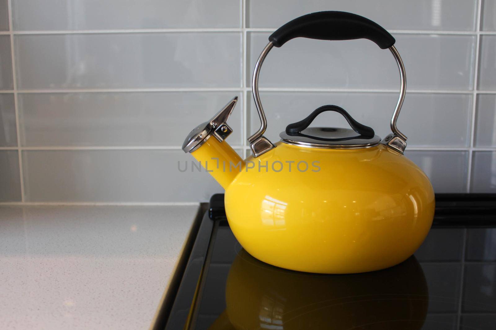 Yellow steel kettle on the gas hob on the wooden table. Modern yellow teapot on the stainless steel
