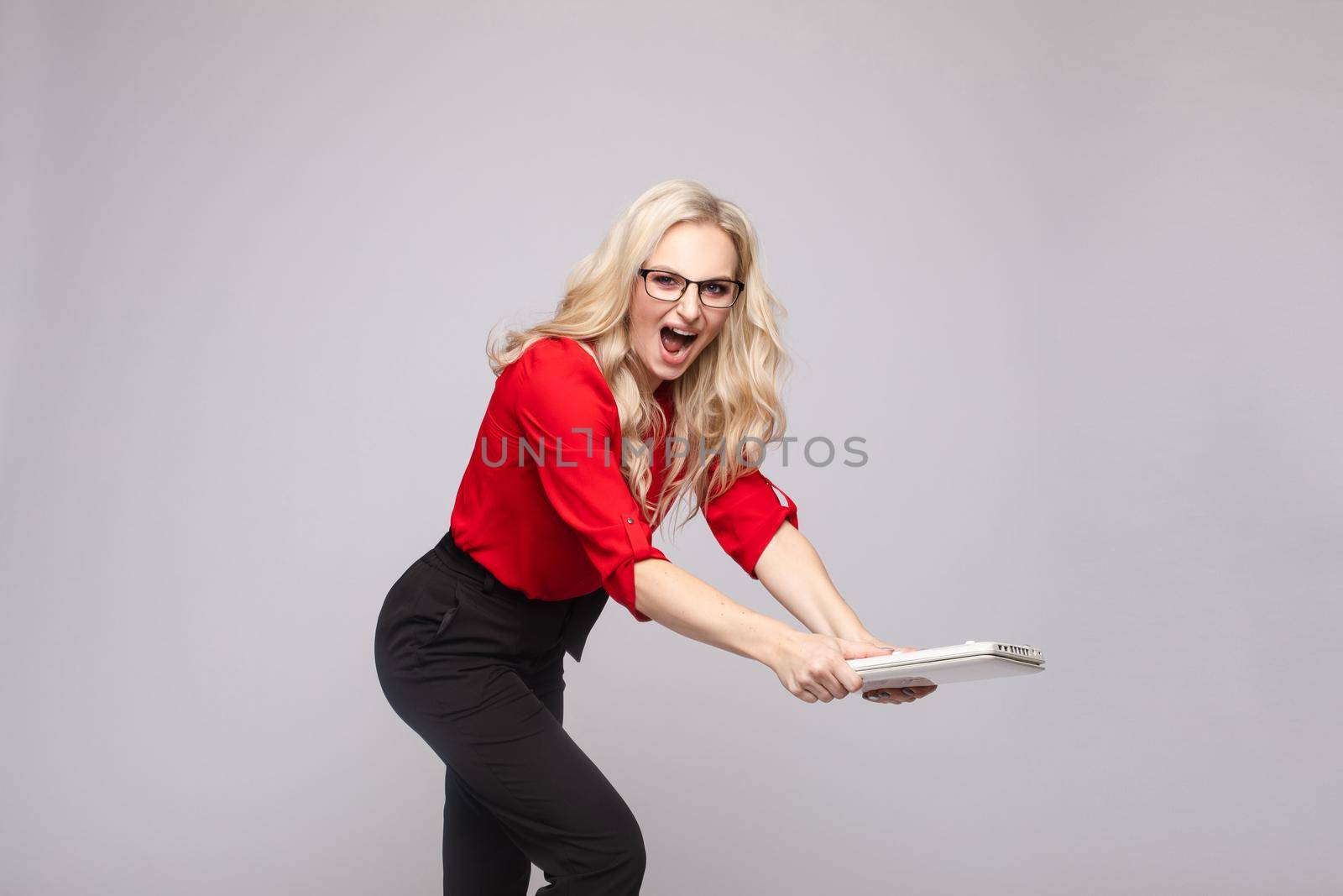 Side view of angry female manager crashing computer and shouting on white isolated background in studio. Furious woman in glasses irritating while working. Concept of problems and troubles.