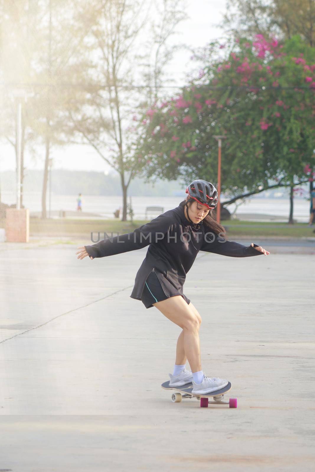 Asian women on skates board outdoors on beautiful summer day. Happy young women play surfskate at park on morning time. Sport activity lifestyle concept
