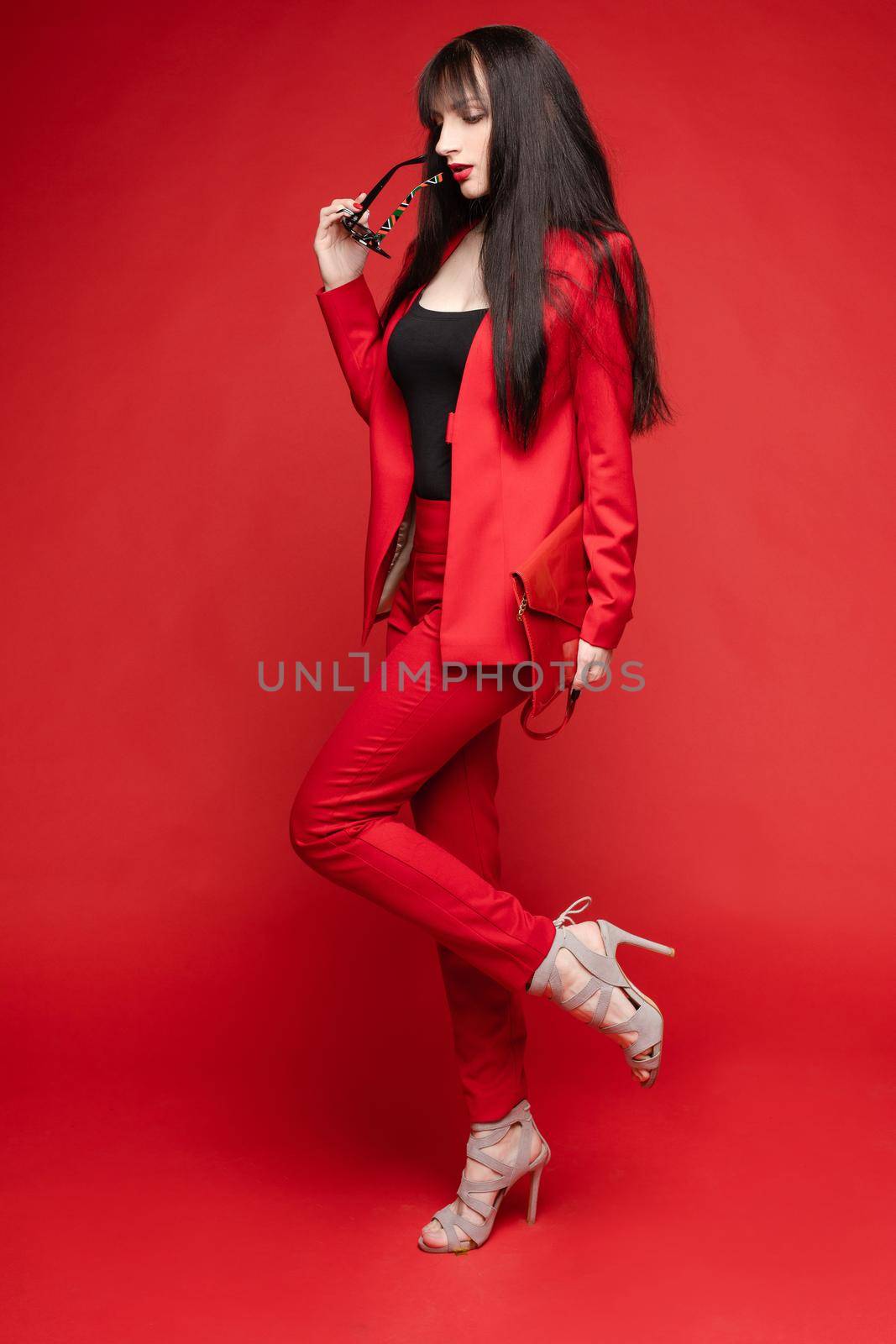 Side view of glamorous brunette posing in red smart suit by StudioLucky