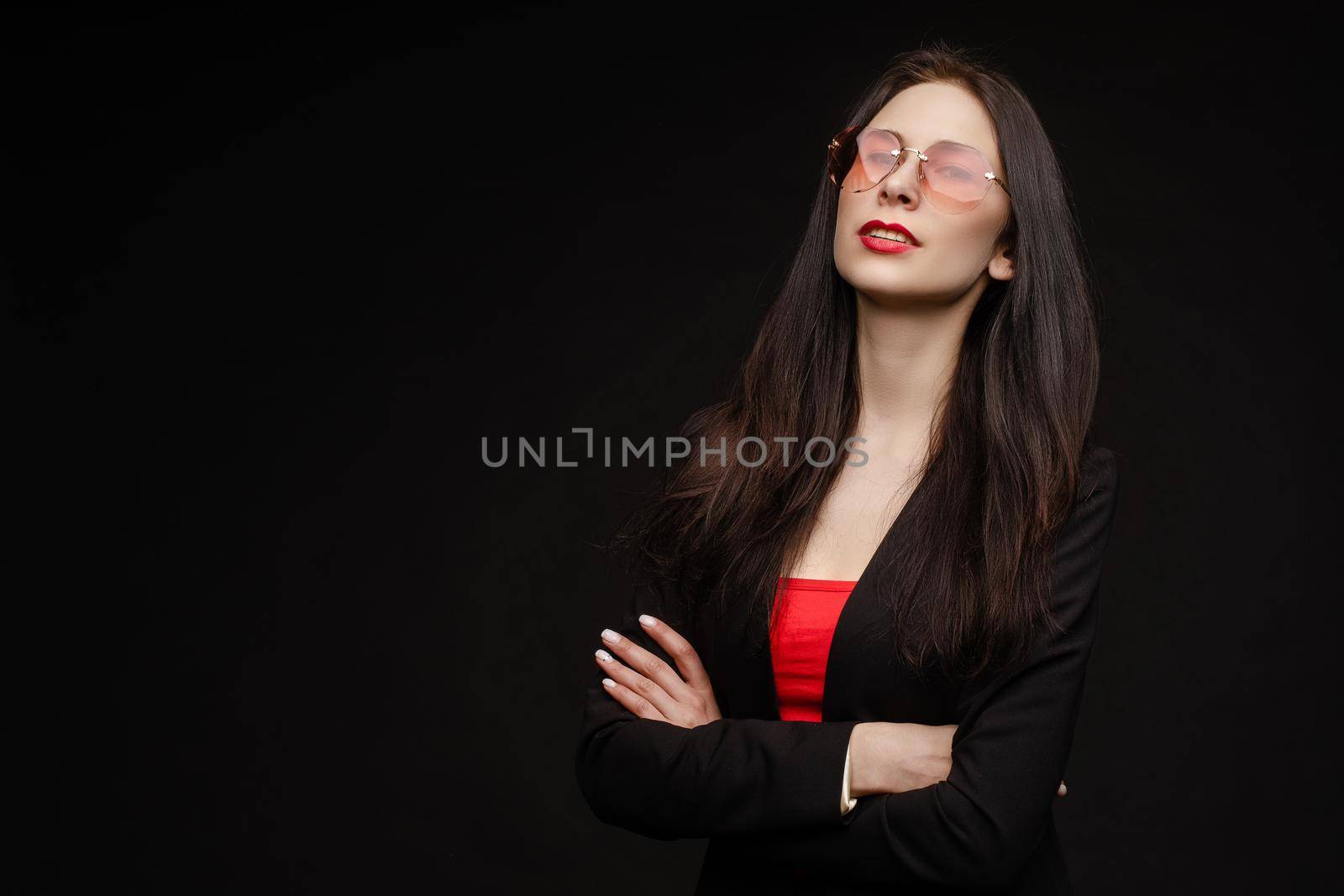 Portrait of young beautiful woman thoughtfully looking down. Brunette model in elegant costume posing at camera . Pretty lady in red sunglasses leaning one hand on other and holding it near face.