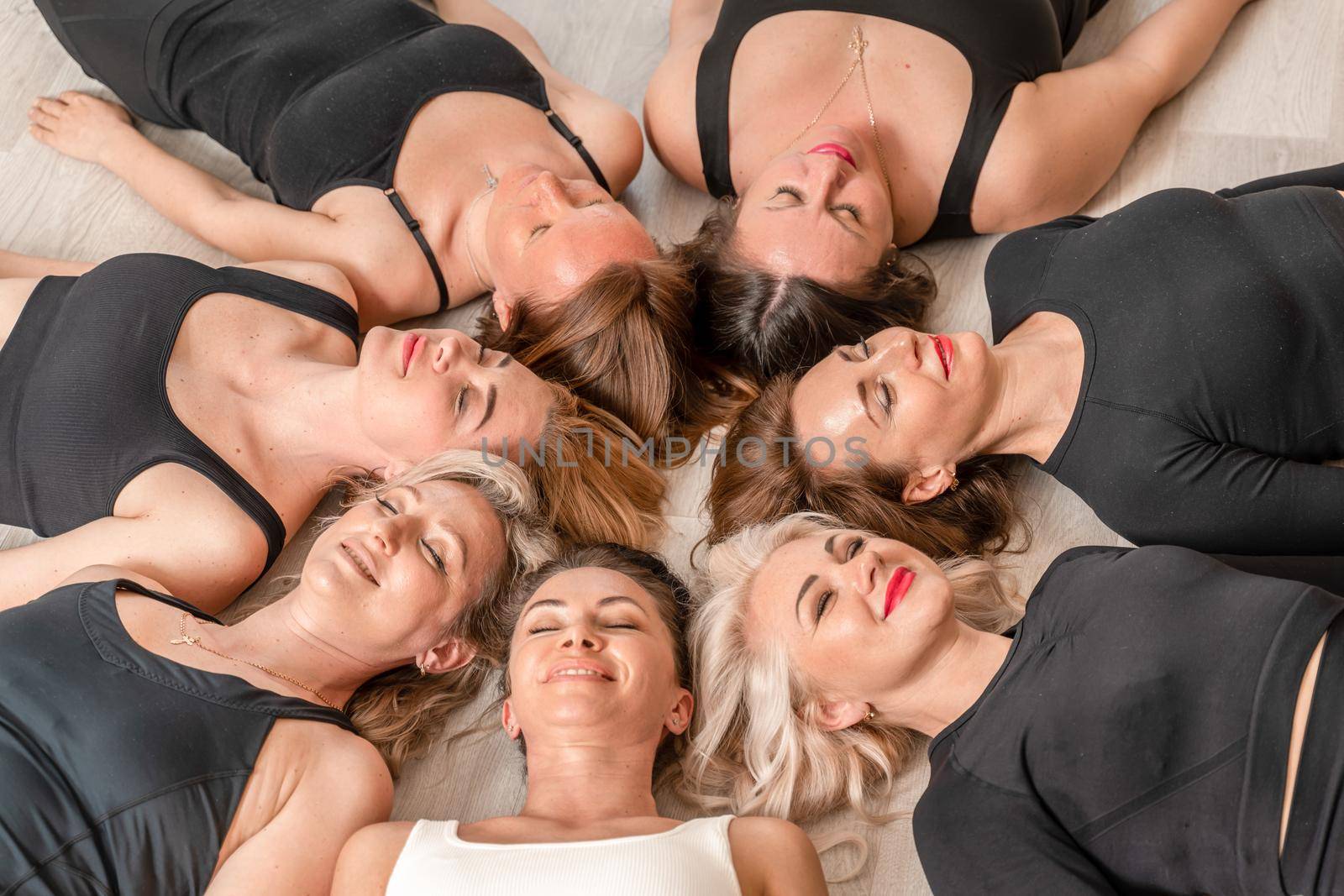 Seven happy women lie on their backs on the floor with their hea.