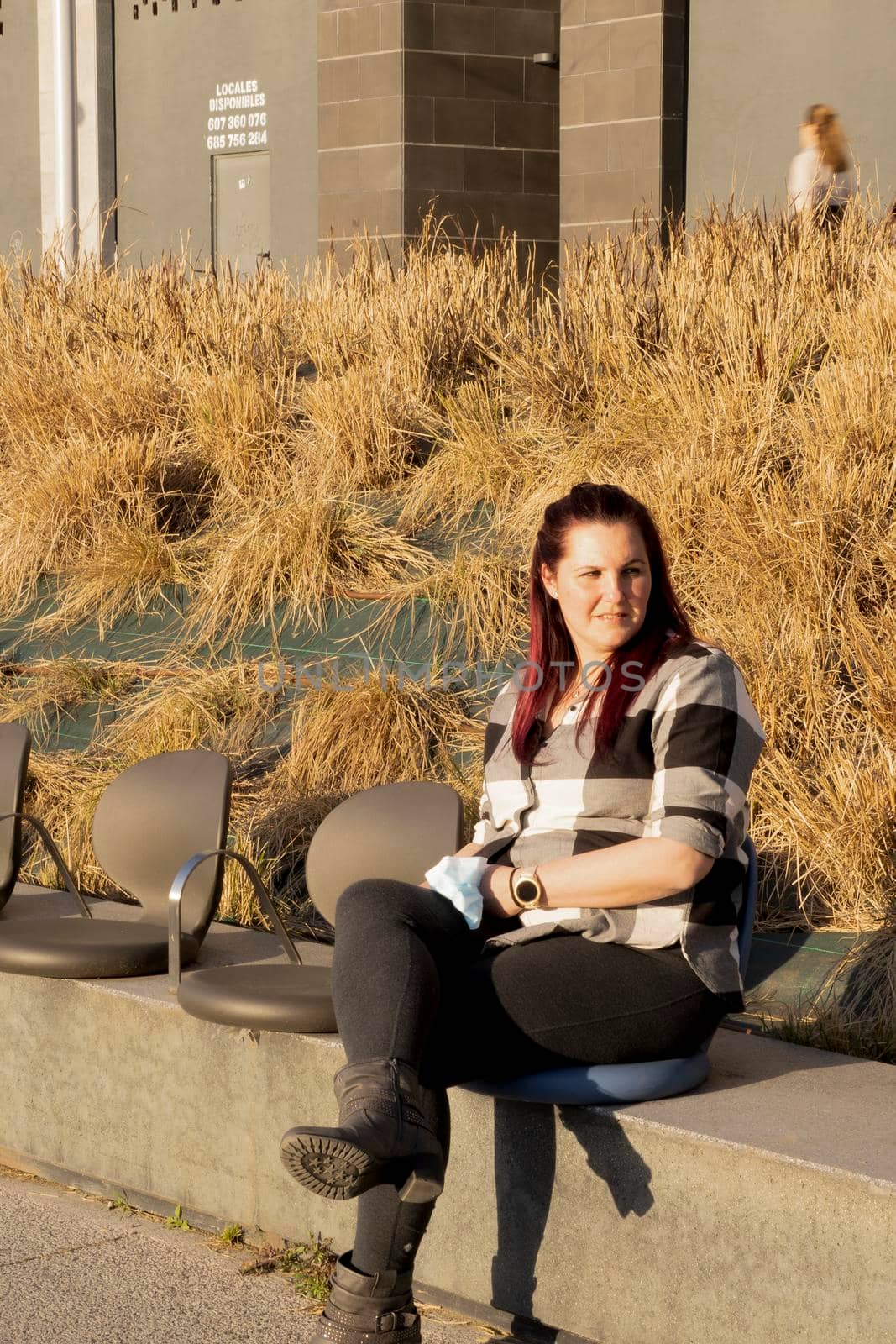 Young woman posing sitting on a bench, wearing a plaid shirt and reddish hair. casual look