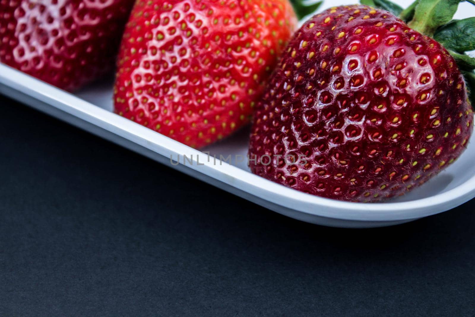 Strawberry in a white plate close up on a black background. Fresh red strawberry in white bowl on black background. side view, copy space, close up.