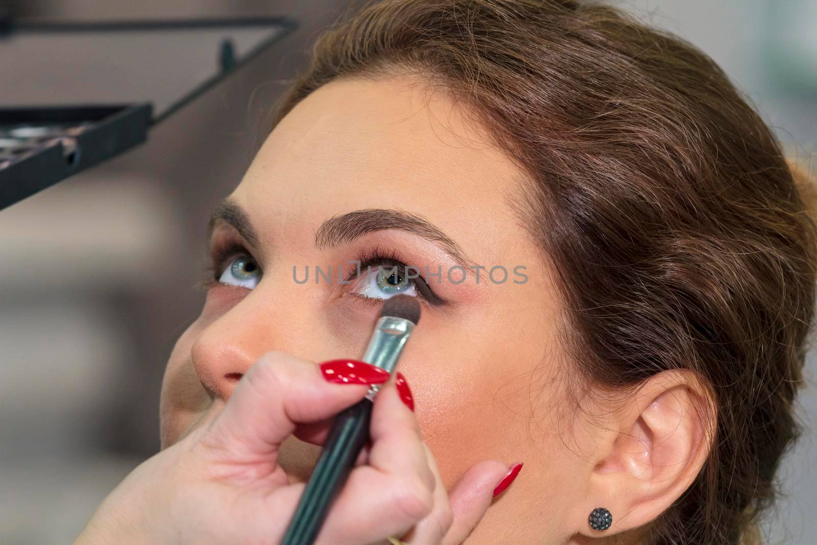 Master stylist makes eye makeup for a girl in a beauty salon.