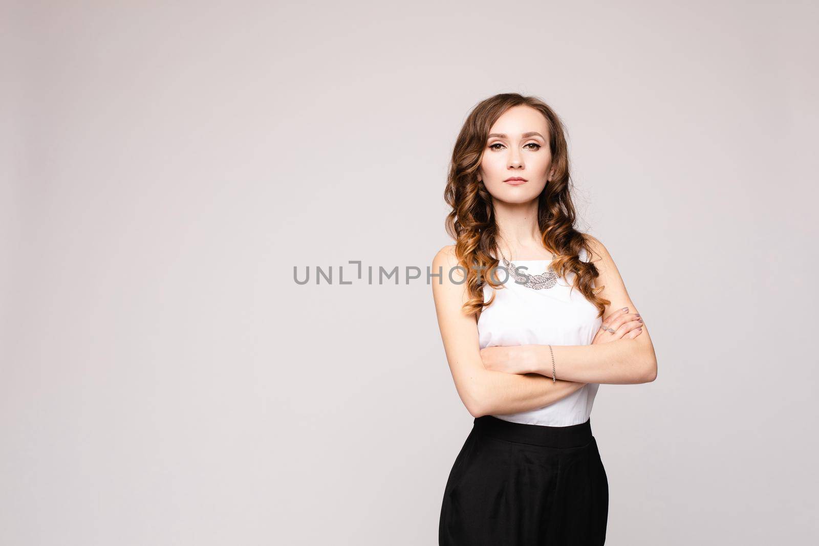 Front view of elegant successful female wearing smart outfit and glasses and posing on isolated background. Intelligent woman with folded arms looking at camera in studio. Concept of job and business.