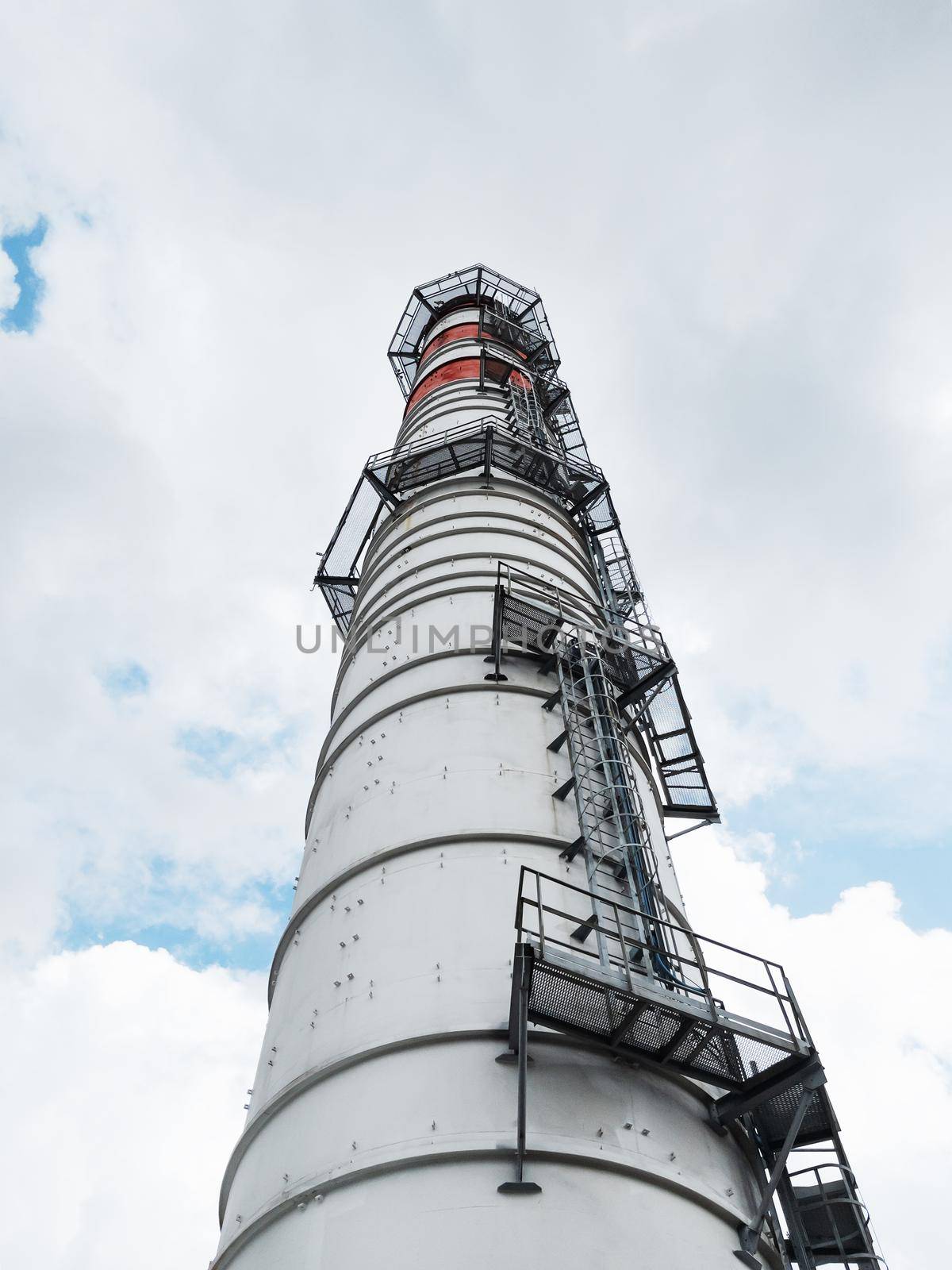 White chimneys of a power plant on a background of clouds with diagonal lines in a vertical frame