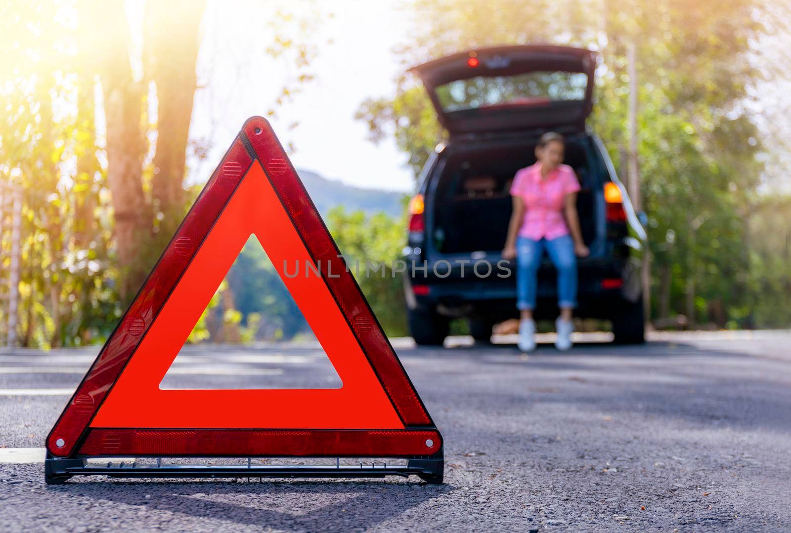 Close up red emergency stop sign standing on road. Worried and angry woman walking near his broken car talking on phone with insurance agent. Close up triangle on side road