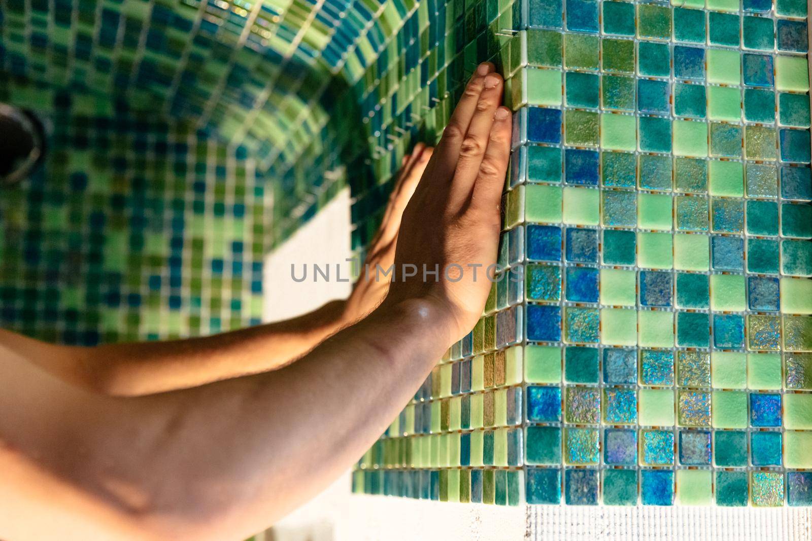 Worker applying mosaic tiles in bathroom, sauna walls. Construction tools and equipment. Spa or sauna relaxation modern room interior design. Adhesive for mosaic tile. Renovation concept.