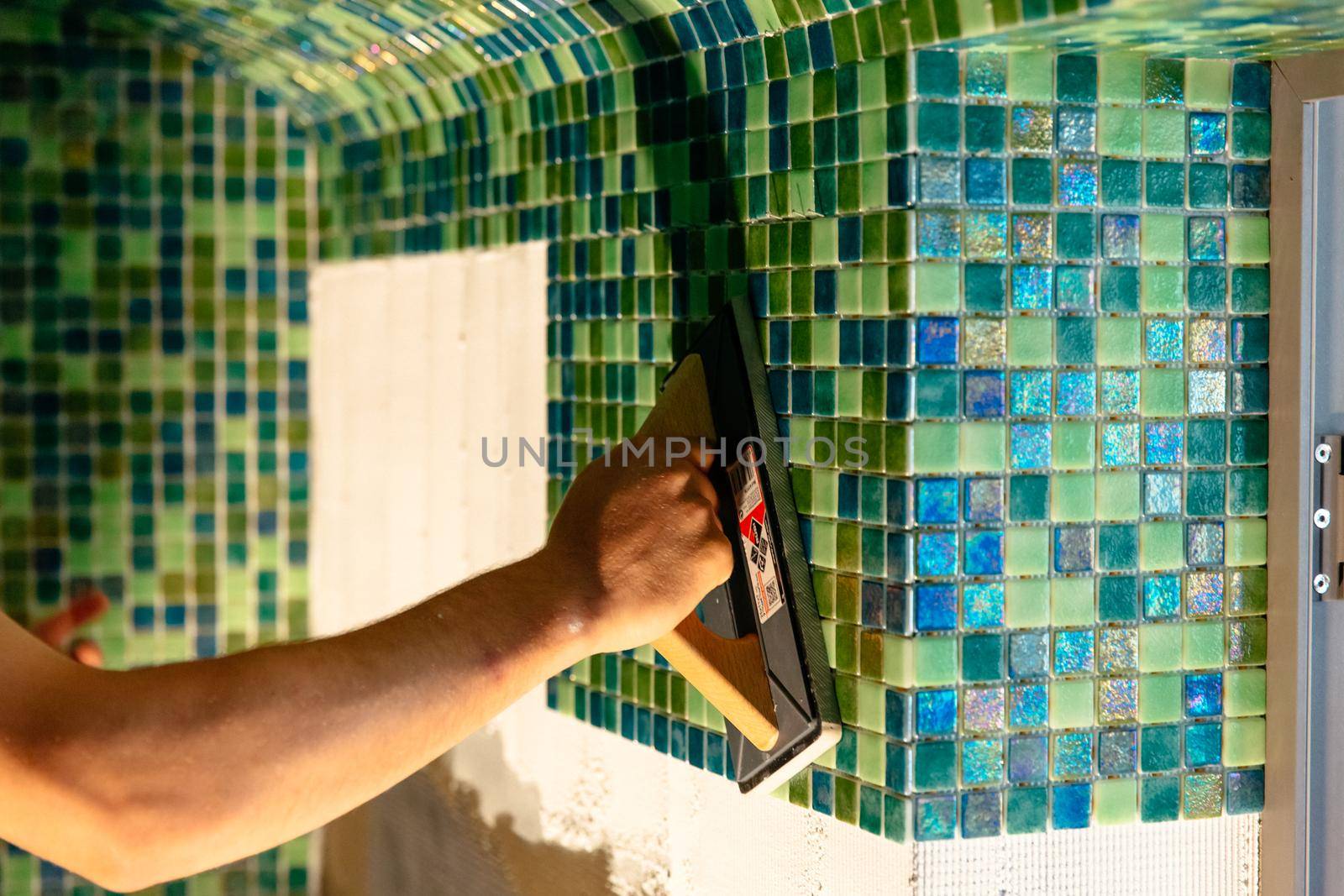 Worker applying mosaic tiles in bathroom walls. Spa or sauna relaxation modern room interior design.