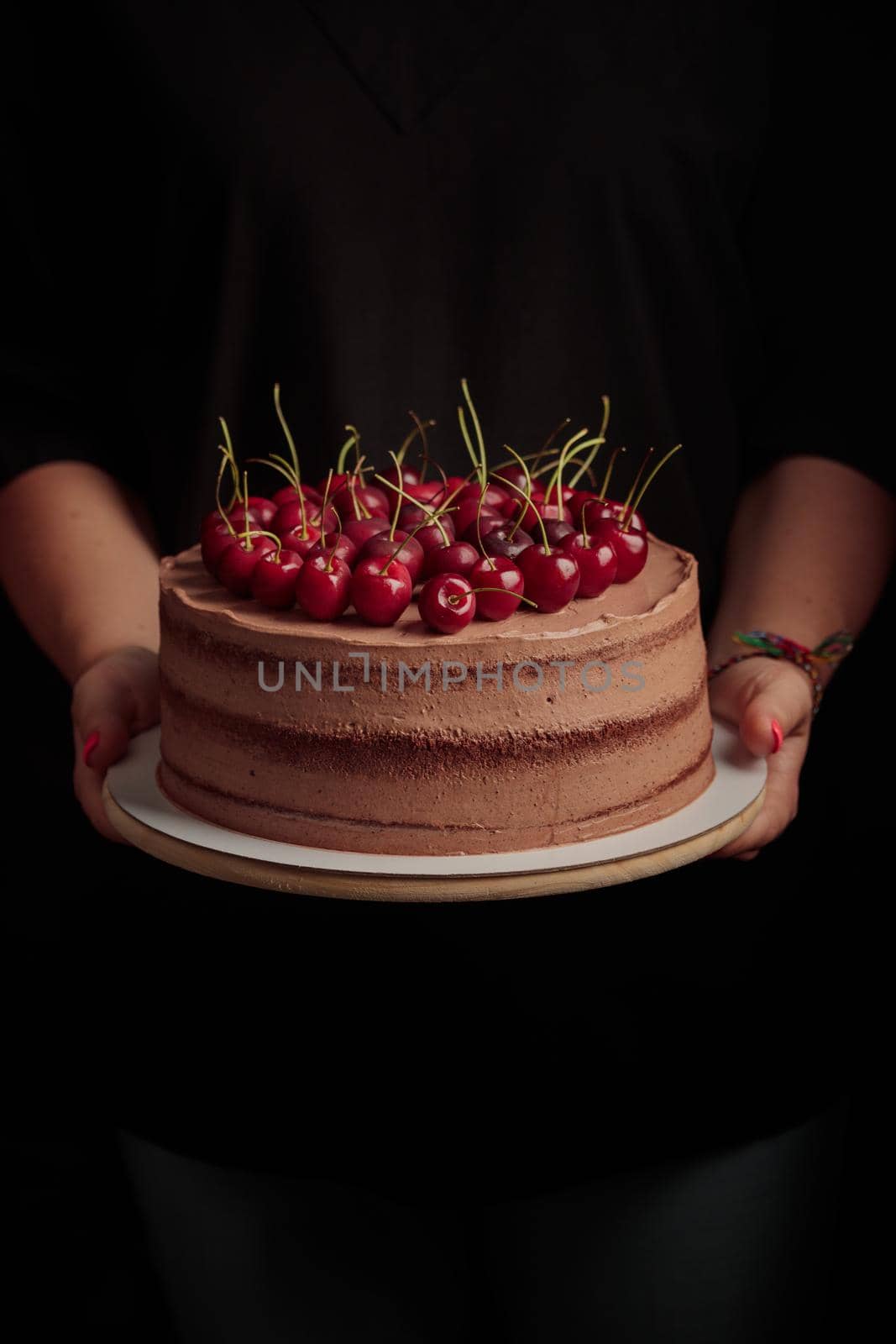 Cake with berries in woman's hands on a black background