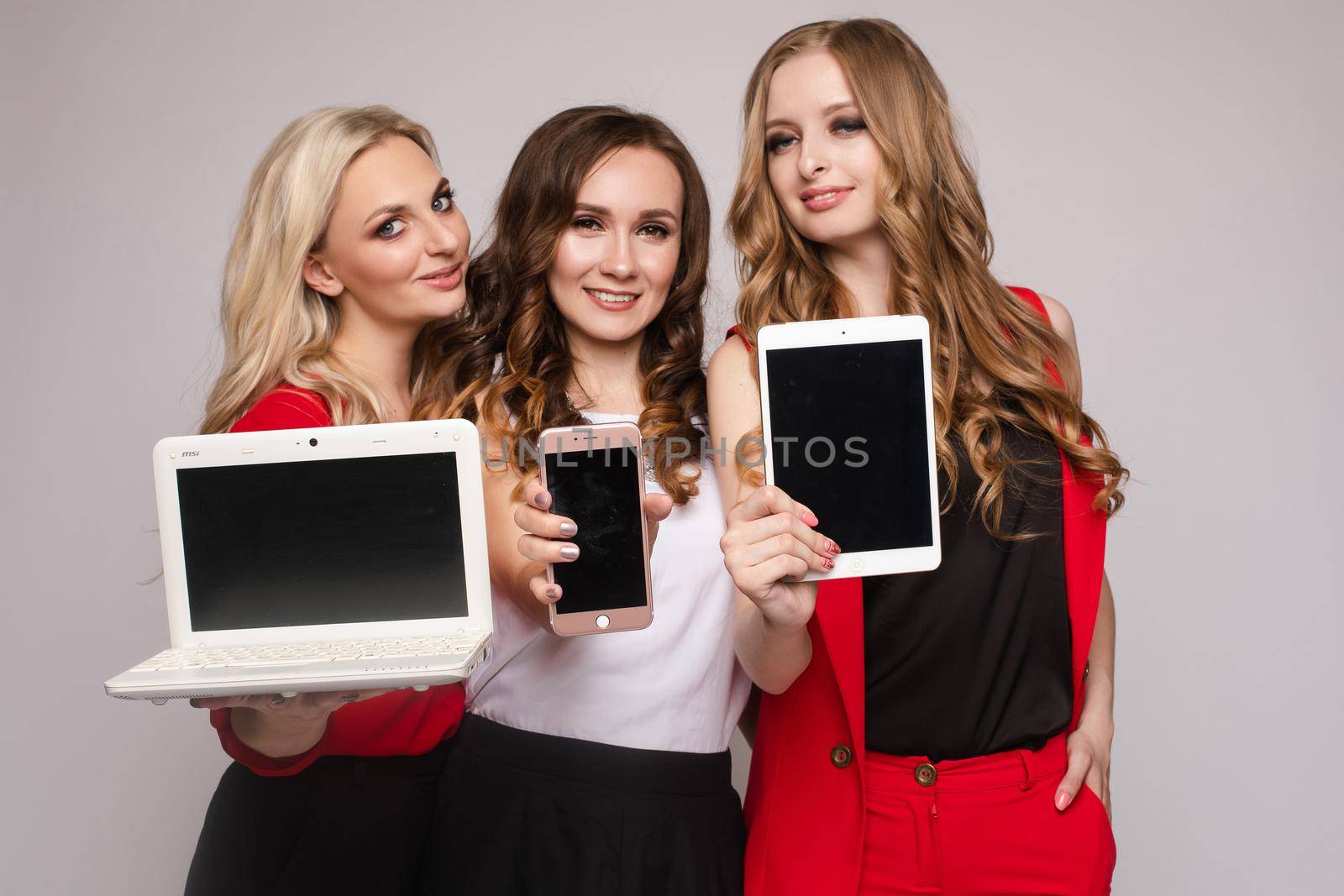 Three gorgeous elegant young women in casual clothes using laptop, mobile phone and tablet. They are using gadgets for work and communication.