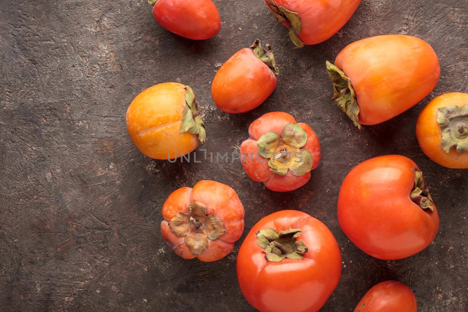 Different fresh persimmons on a dark background