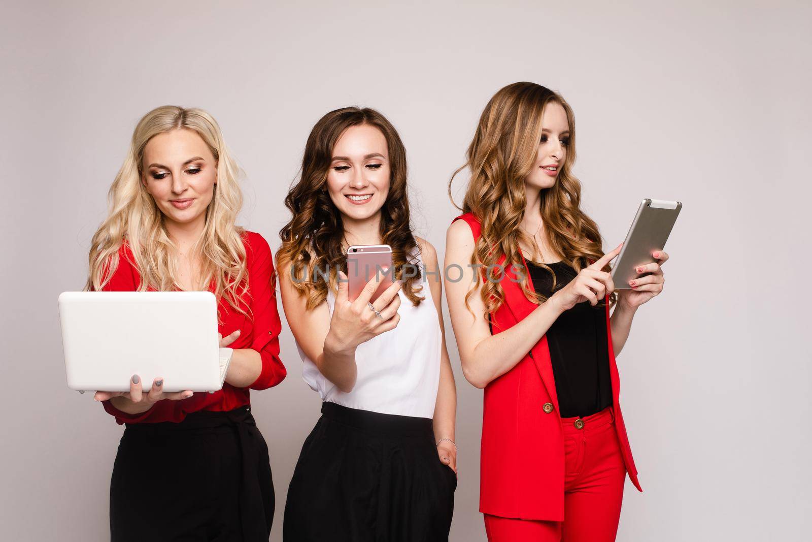 Three ladies using gadgets. Three gorgeous elegant young women in casual clothe by StudioLucky