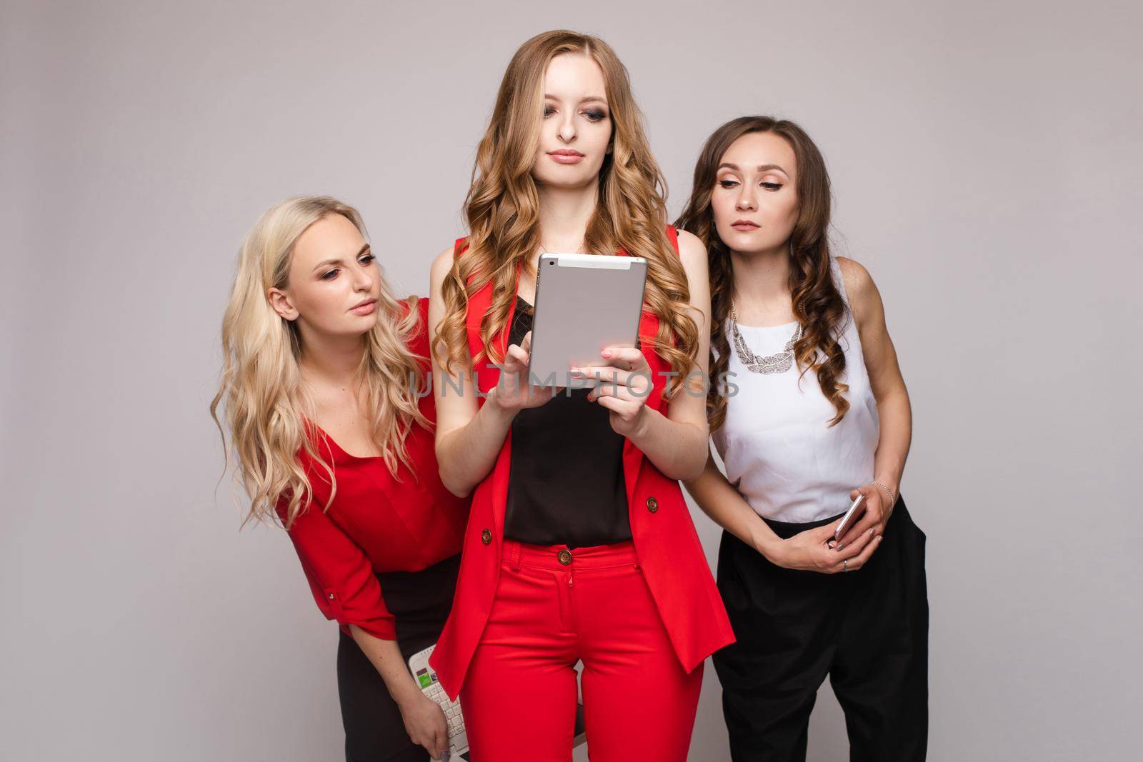Three ladies using gadgets. Three gorgeous elegant young women in casual clothe by StudioLucky