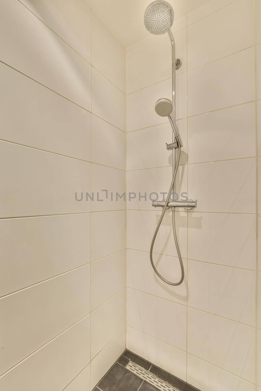 Shower faucets attached to tiled wall near glass partition and ornamental curtail in washroom at home