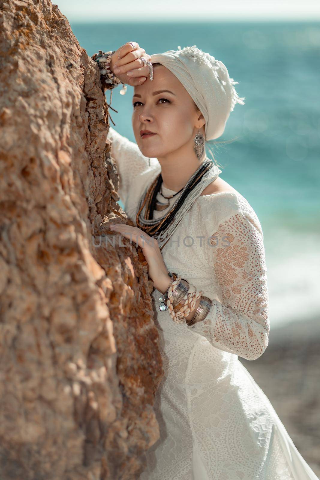 Middle aged woman looks good with blond hair, boho style in white long dress on the beach decorations on her neck and arms