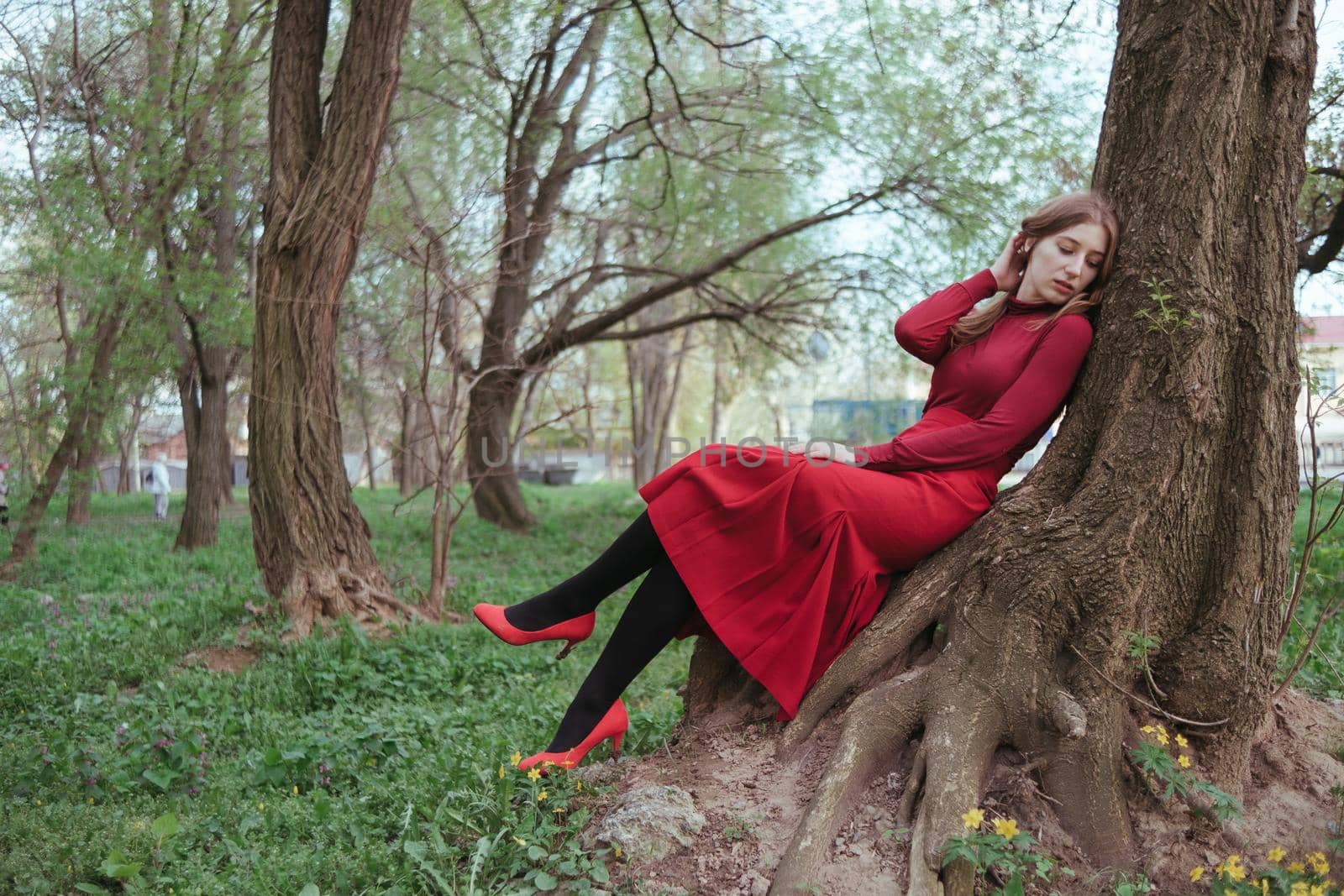 a girl in red rests leaning on a tree in the spring forest