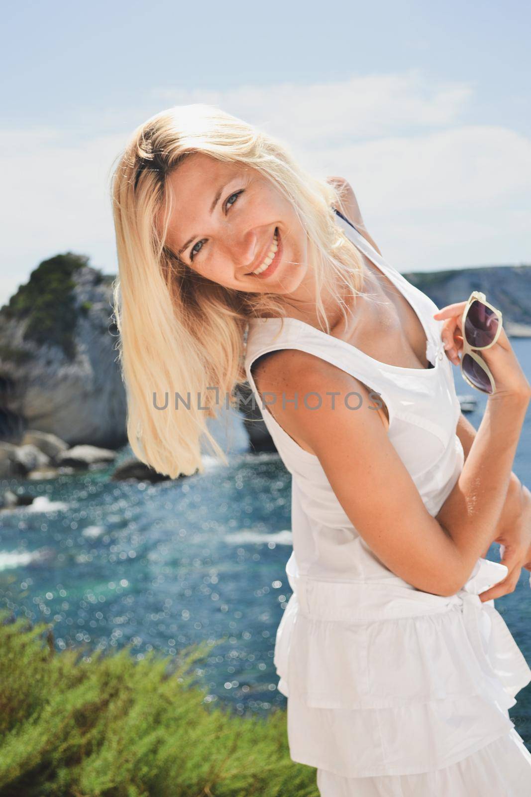 Blonde woman in white dress smiling near the sea by Godi