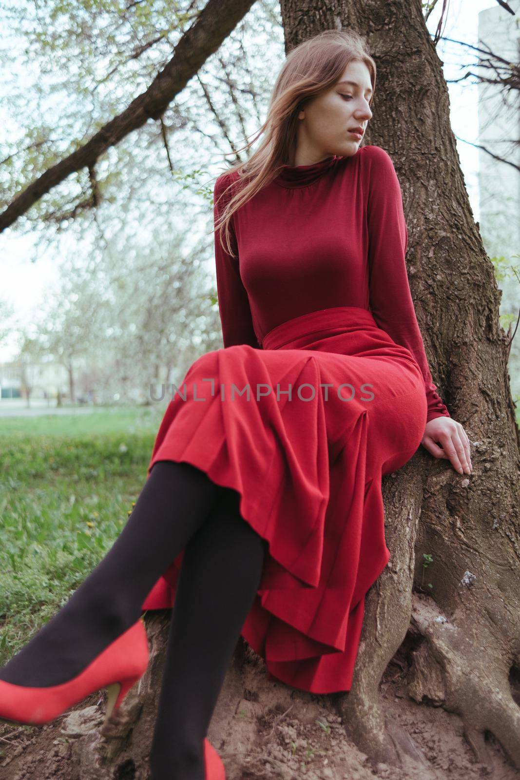 a girl in red sits under a tree in the spring forest and enjoys nature