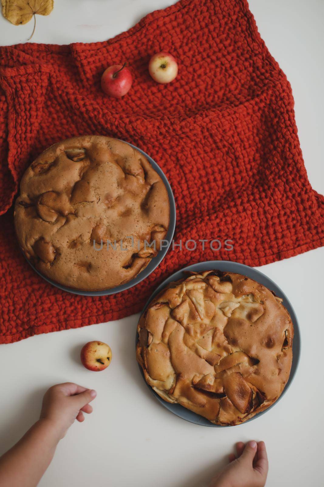 Baby hands reach for the apple cake on white table top view.