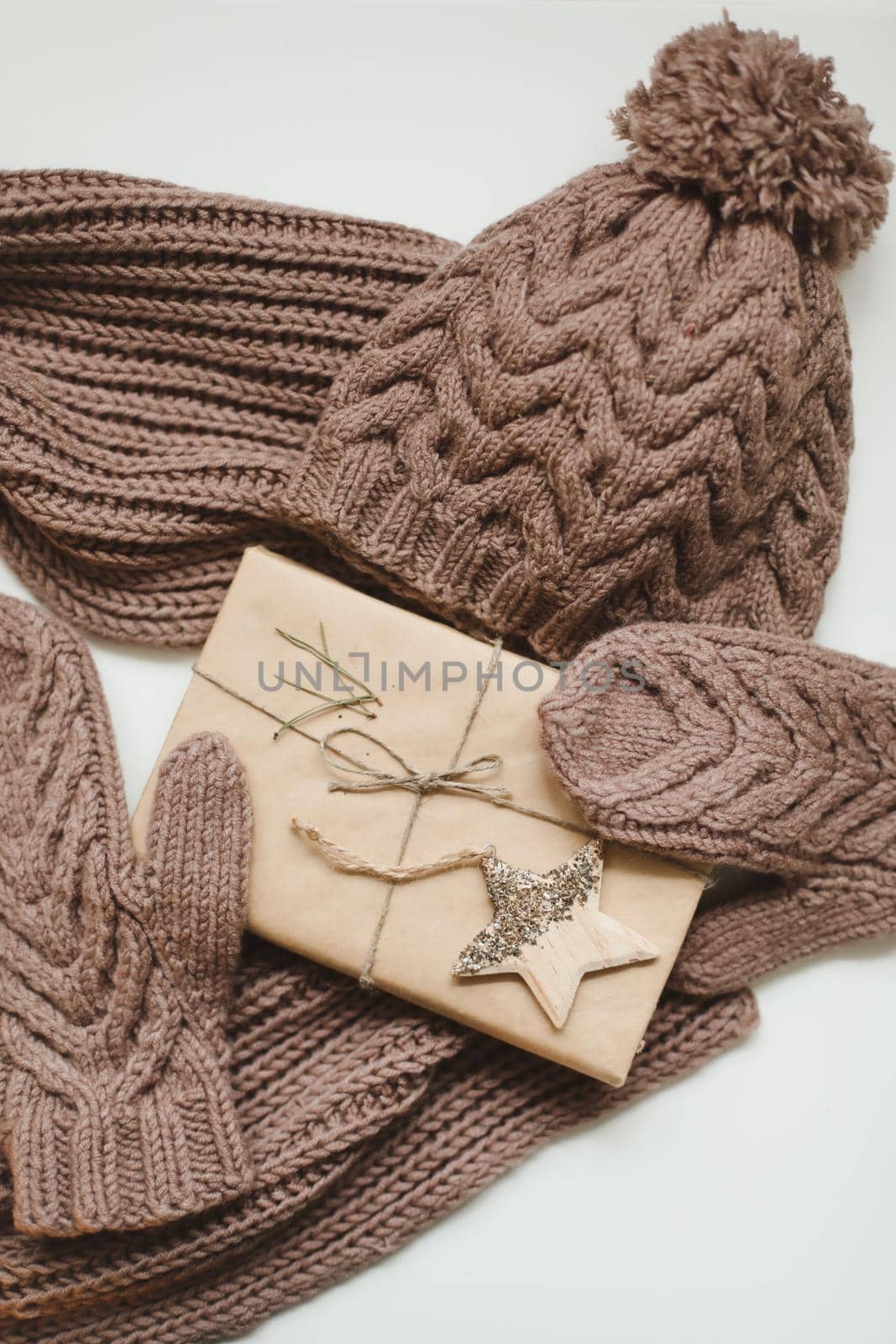 Knitted hat, scarf and mittens and a Christmas gift wrapped in kraft paper on a white table. High quality photo