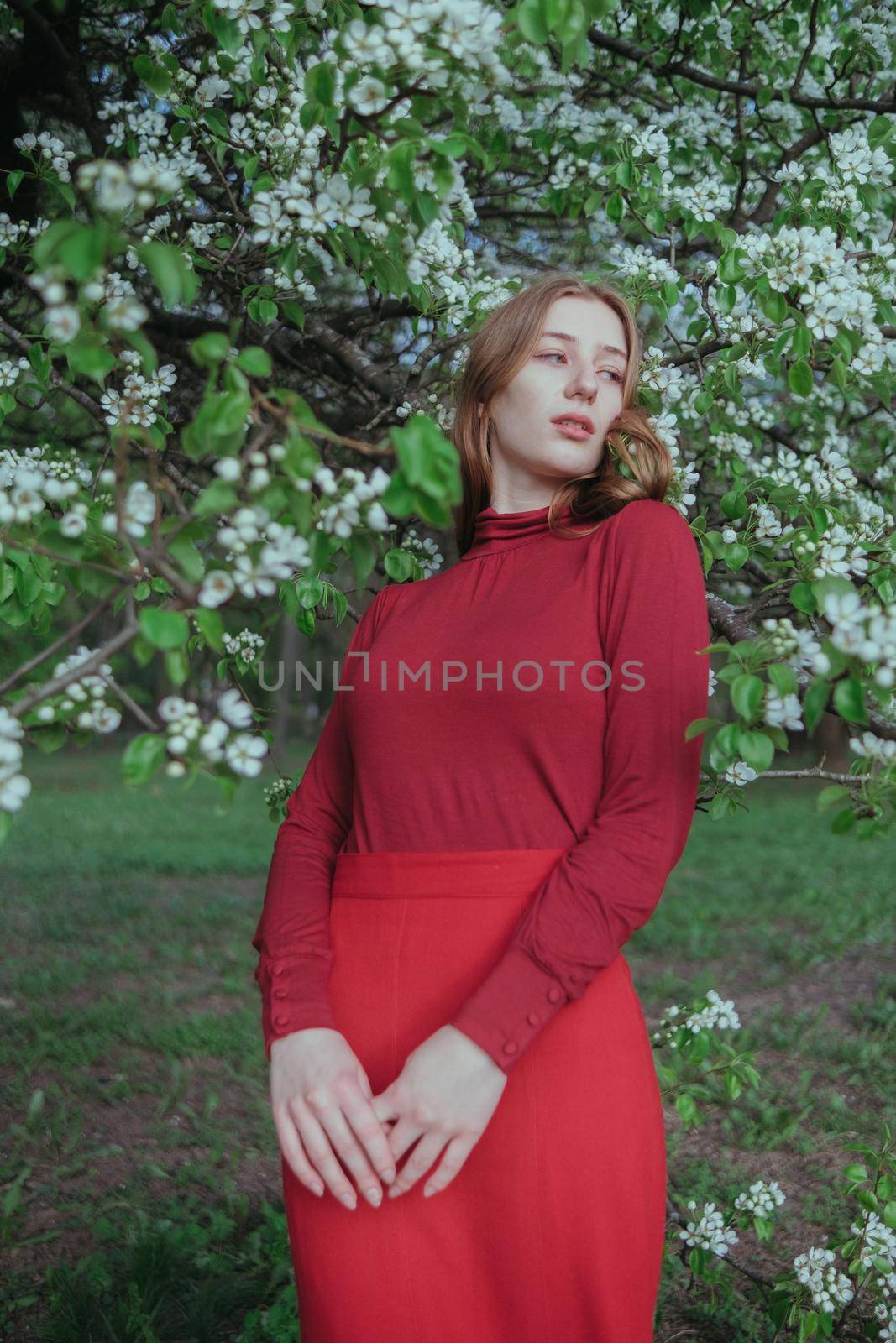 a blonde girl in red unites with nature in a garden of flowering trees by Symonenko