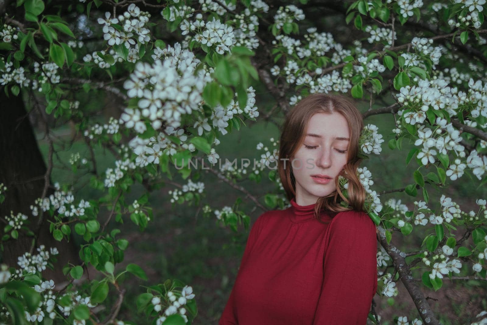 a blonde girl in red unites with nature in a garden of flowering trees