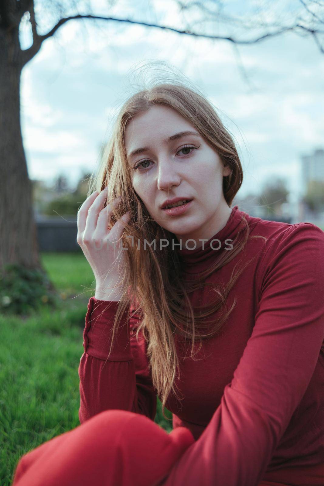 a blonde girl in red sits in the city, her hair is developed by the wind