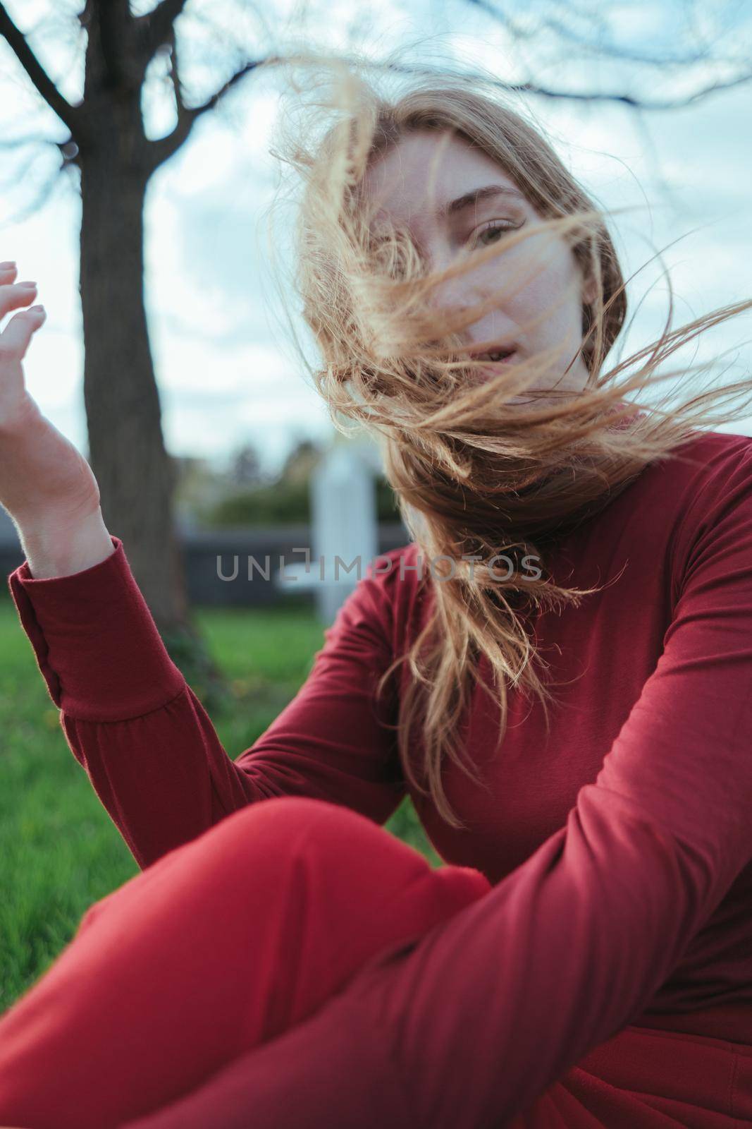 a blonde girl in red sits in the city, her hair is developed by the wind