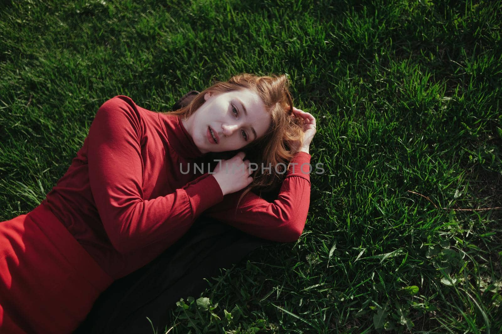 a blonde girl in red lies on the grass in the summer and enjoys the weather by Symonenko