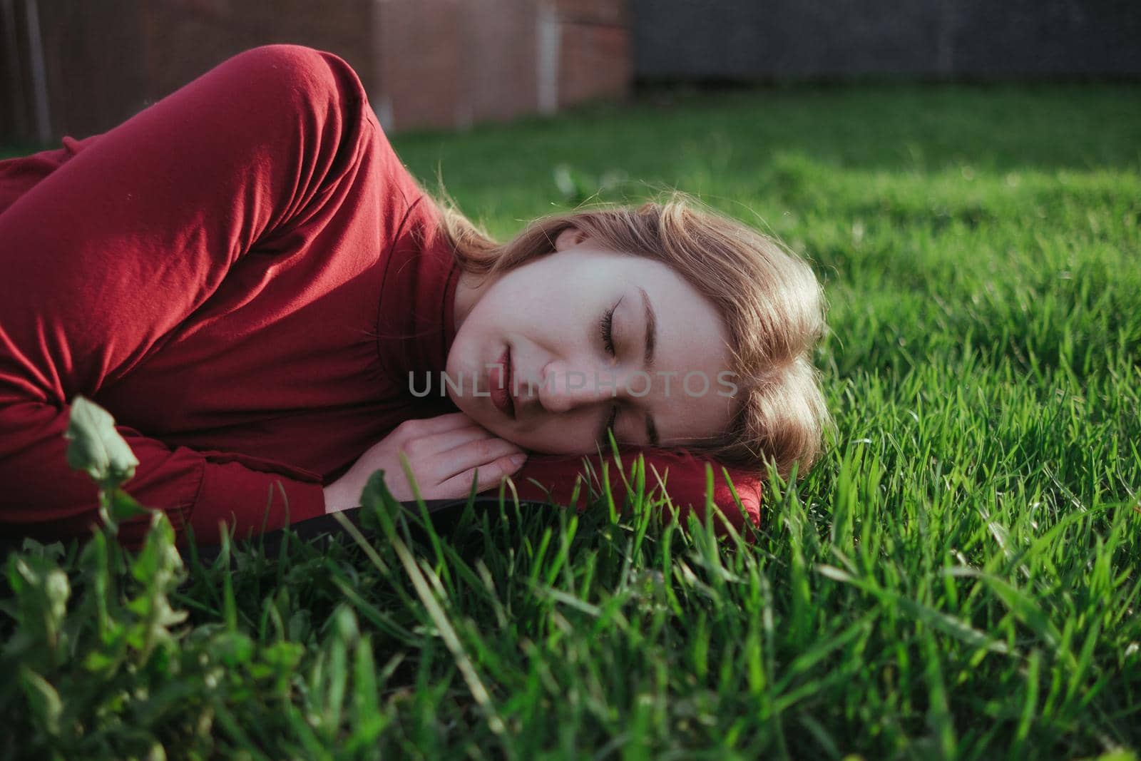 a blonde girl in red lies on the grass in the summer and enjoys the weather