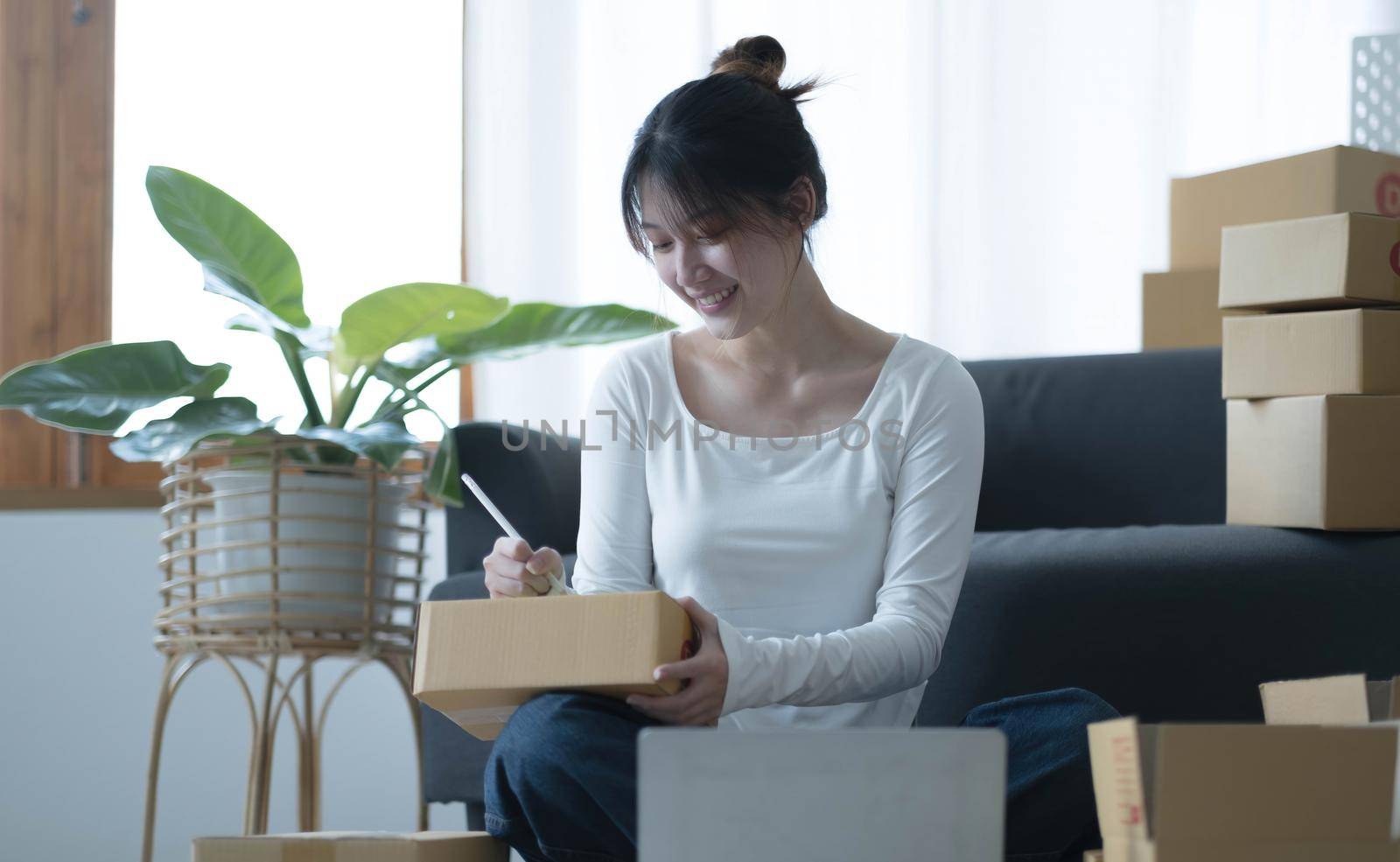 Smiling young Asian business owner woman prepare parcel box and standing check online orders of product for deliver to customer on laptop computer. Shopping Online concept. by wichayada