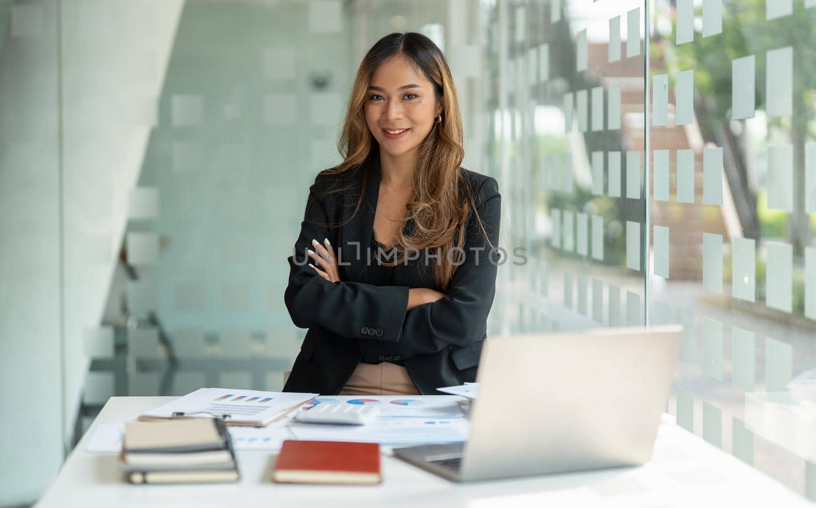 Portrait asian business woman with crossed arms looking at the camera working with laptop computer for accounting financial at office