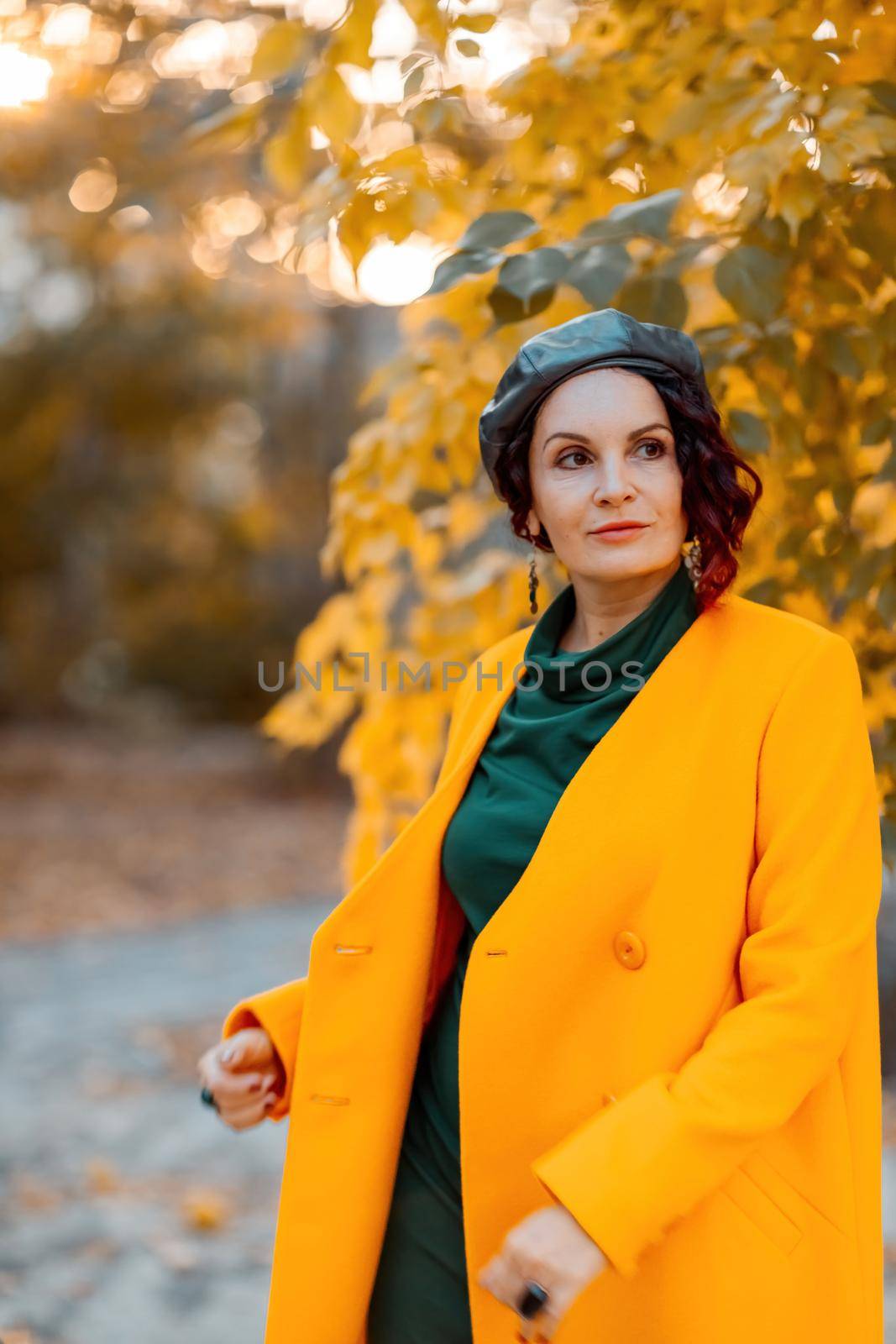 Beautiful woman walks outdoors in autumn. She is wearing a yellow coat and a green dress. Young woman enjoying the autumn weather. Autumn content