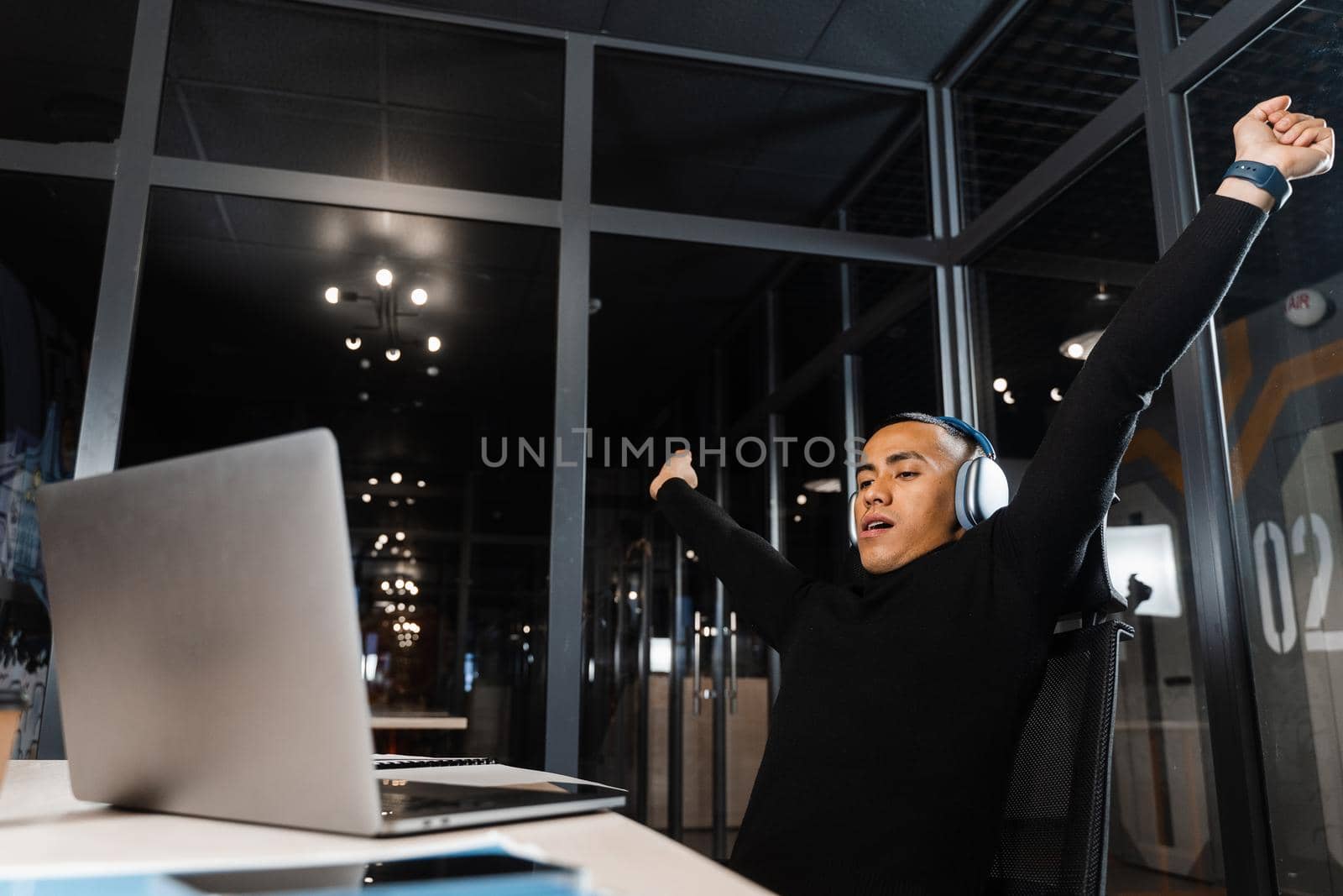 Tired and sleepy Asian man raises his hands up and yawns at the workplace. Work online overtime. Man wants to sleep at work