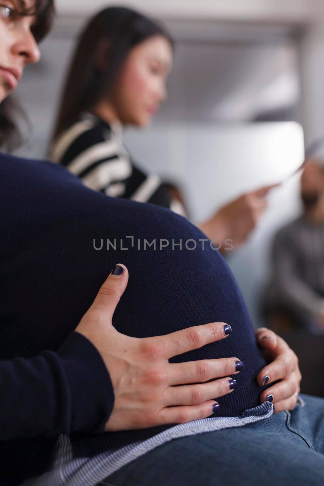 Close up of pregnant manager applicant holding hands on belly bump waiting for job interview meeting in company lobby. Diverse group of recruiters looking at cv resume during recruiting process