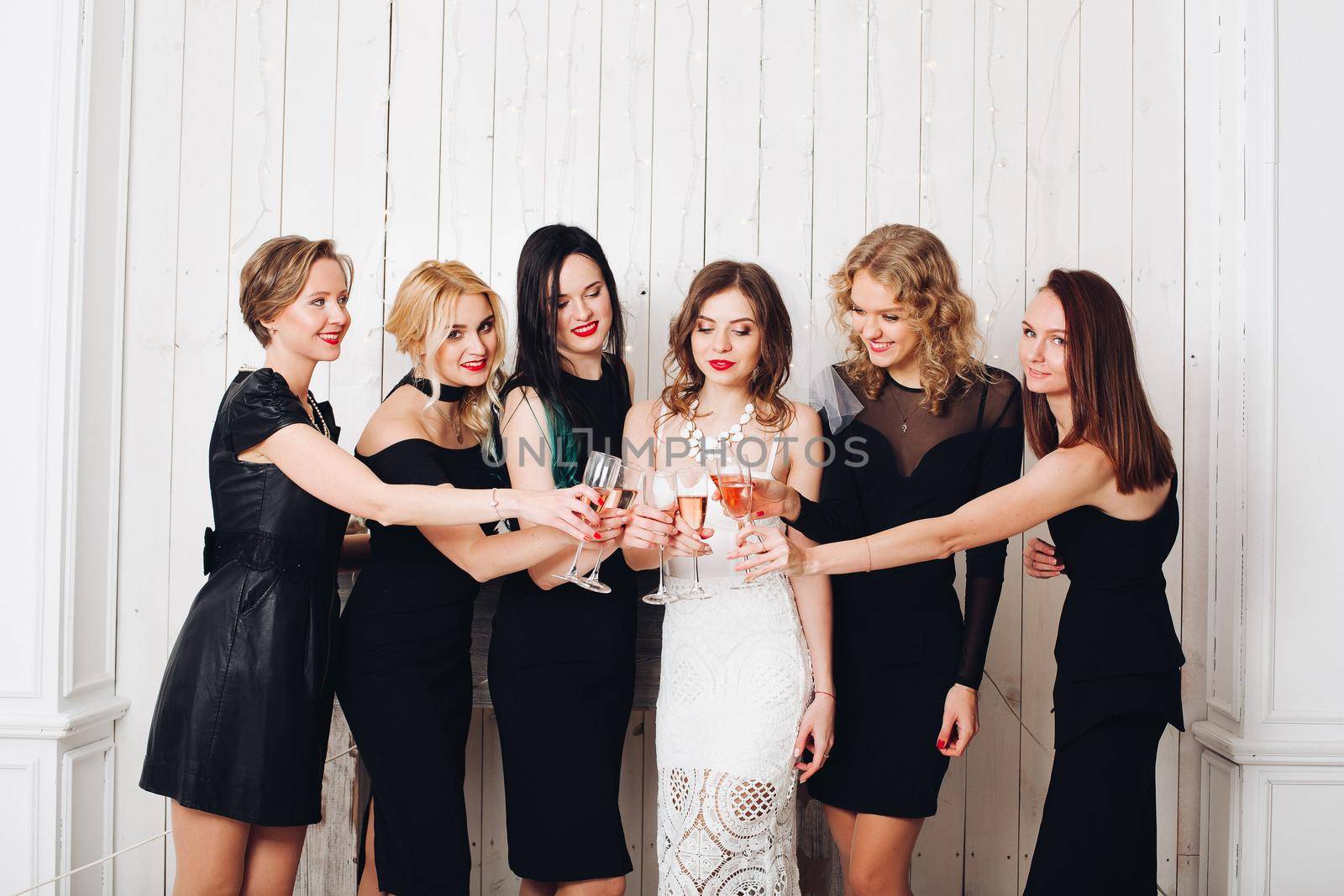 Portrait of beautiful elegant bridesmaids in black dresses toasting glasses of champagne with bride-to-be in lovely white dress.