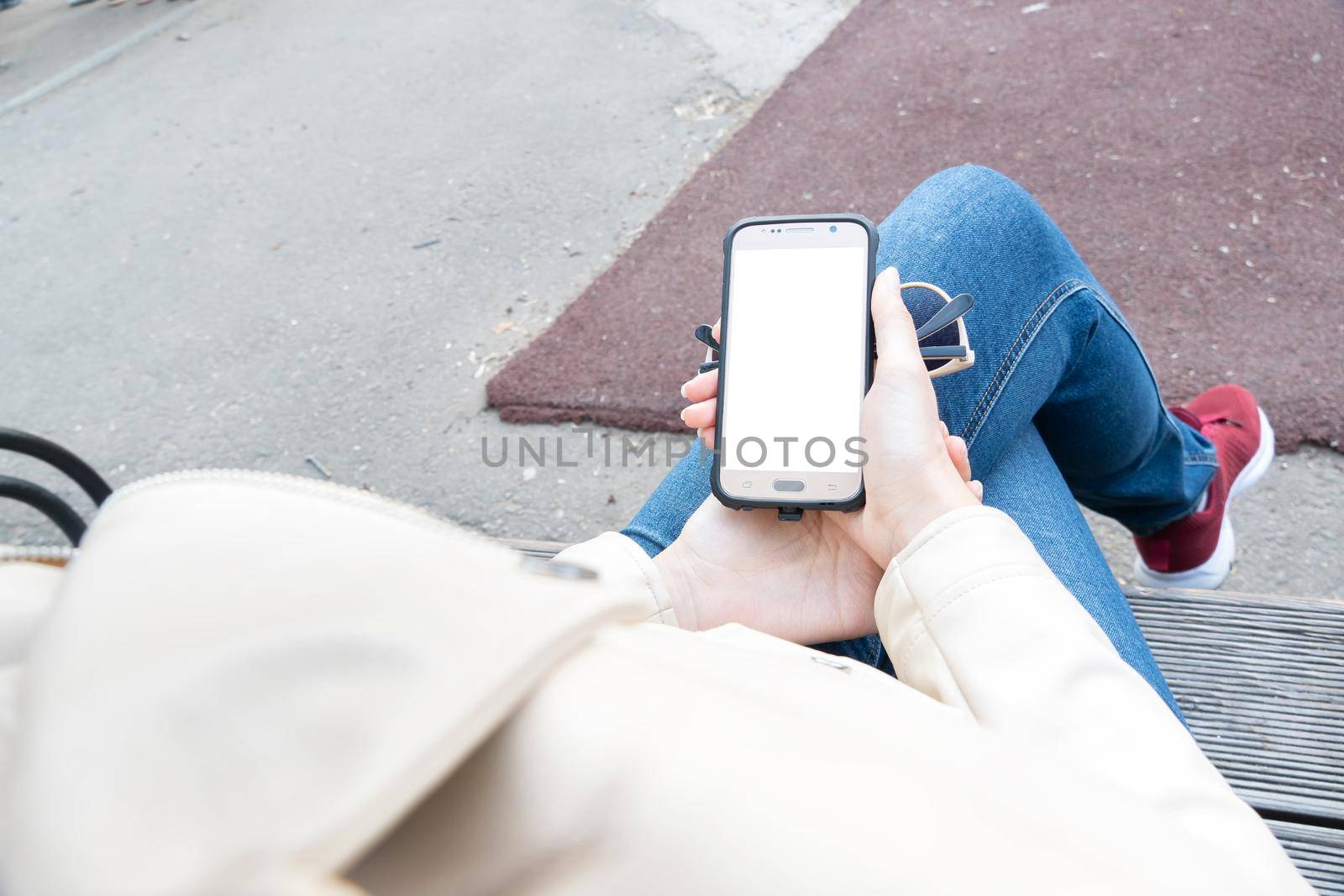 The girl holds in her hand a smartphone with a white screen for your layout or advertising on the phone display.A means of communication,communication and the Internet.Banner,billboard,poster,playbill by YevgeniySam
