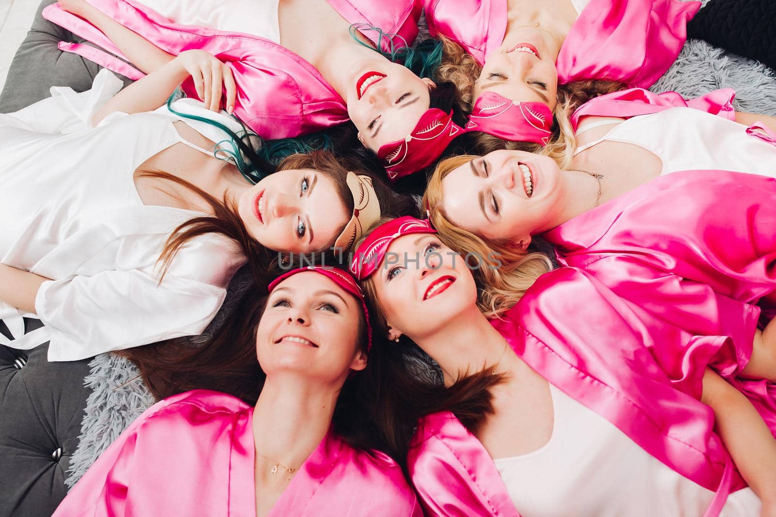 Overhead of attractive young girls in pink robes lying on bed in circle. Bachelorette party.