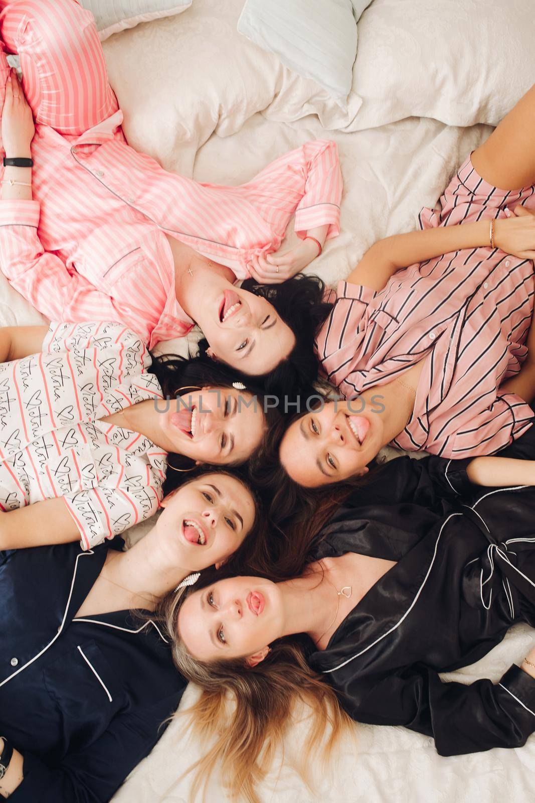 Top view of group of pretty young women in pajamas lying on bed and having fun. Birthday party concept