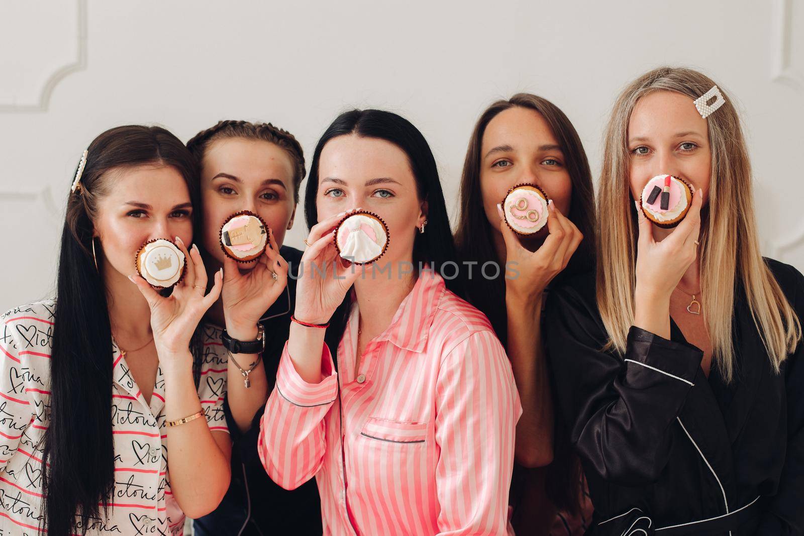 Happy pretty women in sleepwear sitting on the edge of the bed and holding cupcakes. Friendship and happiness concept